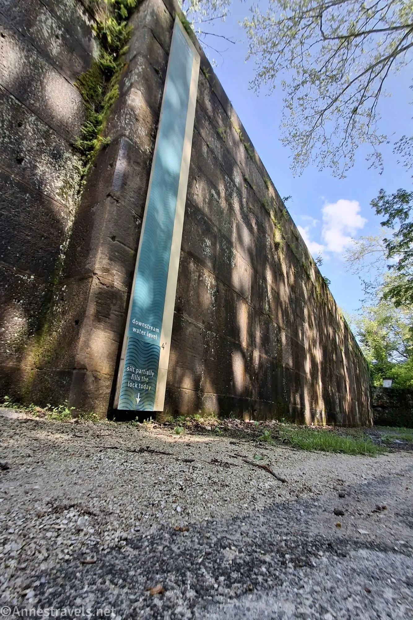 A sign on the wall of an old canal lock with blue sky and trees above 