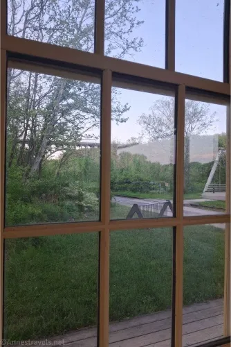 Through a window, we can see trees, a bridge, and a path 
