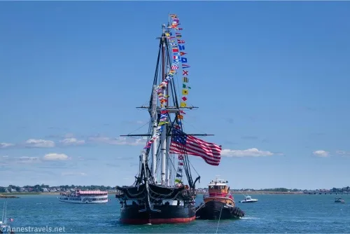 The bow of a historic warship with pleasure boats looking on in Boston Harbor