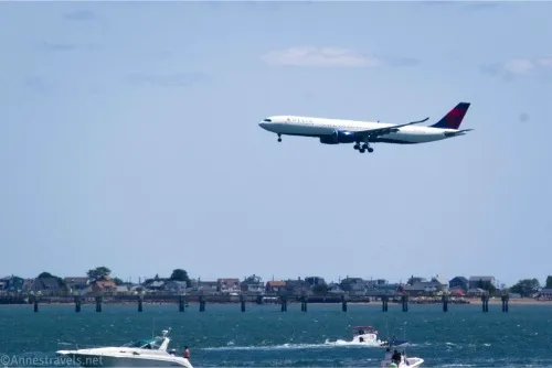 An airplane sails above the water and houses with boats in the water below