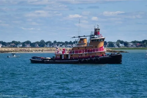 A brown, red, and black tugboat floats in Boston Harbor