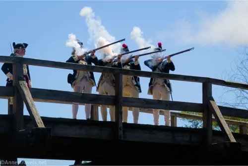 Four men on a bridge fire muskets while their captain watches