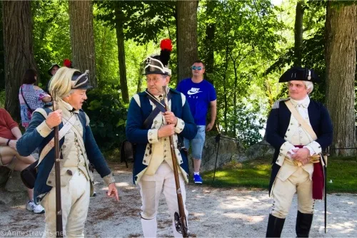 Three men in the costume of Continental soldiers talk together while a man in a blue t-shirt watches