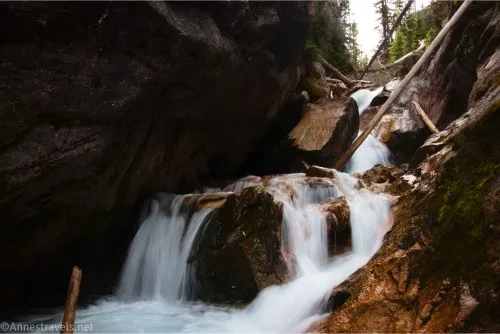 A silky waterfall flows over rocks beneath a rock overhang 