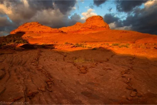 A trail splits in two below a red rock dome and threatening clouds