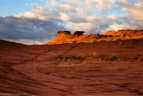 A trail in shadow travels across red rocks while two rock formations and clouds are in the distance