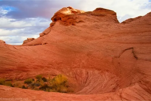 A red rock formation dips into a bowl; clouds sail behind the rock