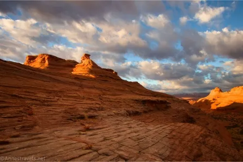 The sun shines on rock formations below white puffy clouds