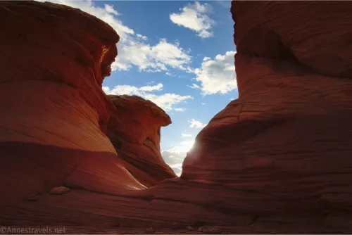 Rock towers rise over a small gap with puffy white clouds in the sky beyond the gap