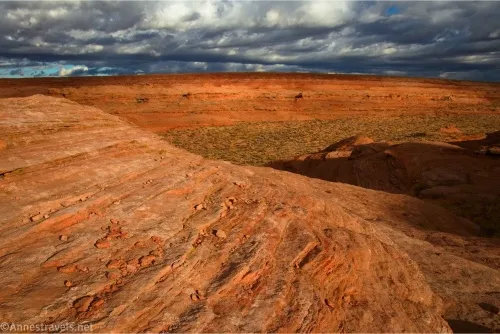 Striped reddish rock dips to a green valley, then rises to another red rock and low-hanging gray-white clouds