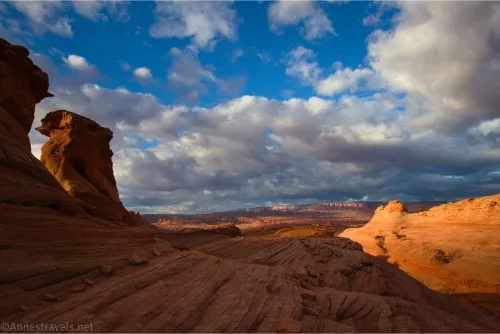 Puffy white clouds hang over the desert while near the photographer are rock formations