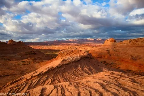 Clouds hang over the desert of red rocks and wave-like layered slickrock