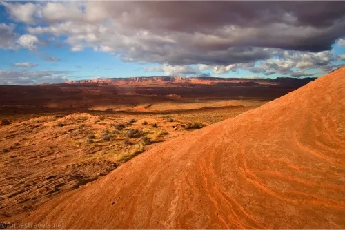 Looking across a redish yellow rock to distant red cliffs under dark clouds