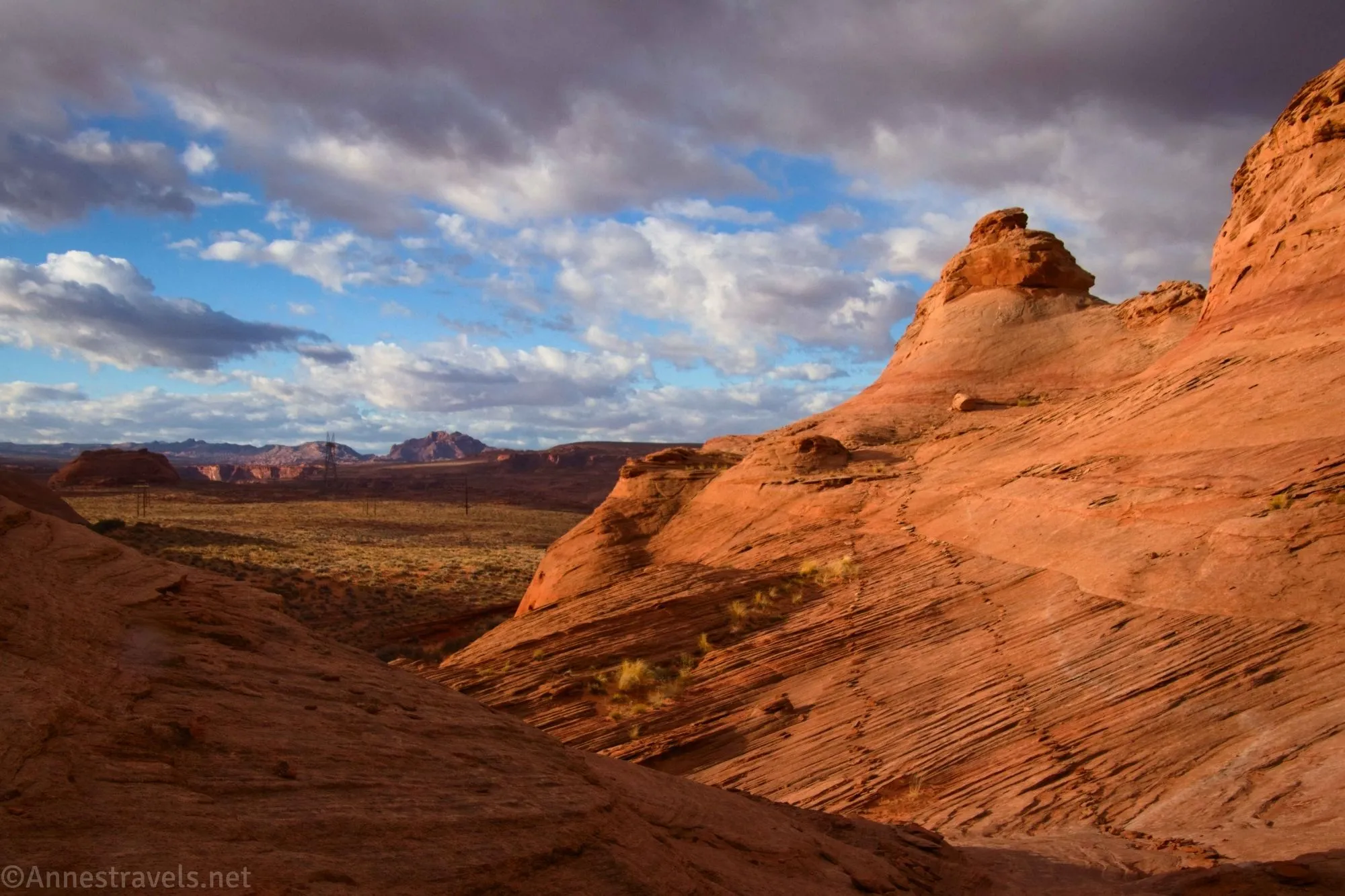 Clouds hang low over a trail across red rocks with views to distant mountains