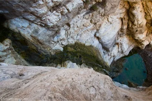 A small trickle of water descends into a green pool between rocky cliffs 