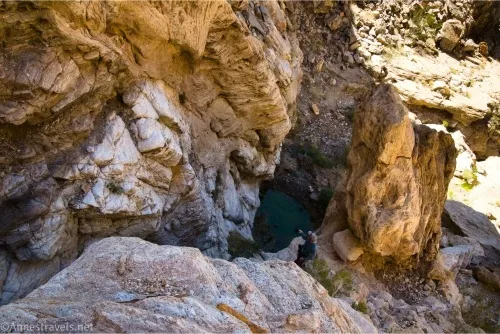 Looking down a rocky cliff to a dark green pool at the bottom of the cliff