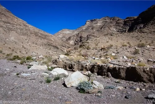 Rocks sit in the gravel of a desert wash with the striped and rugged mountains beyond 