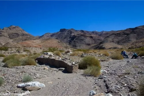 A dry, gravely desert wash splits in two with dry desert mountains beyond