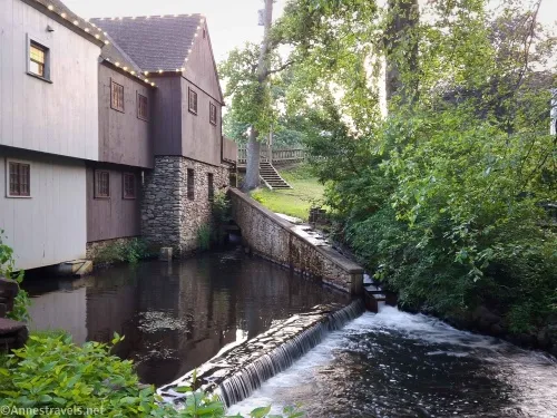 A wood and stone building with lights on the roof with a small waterfall and flume 