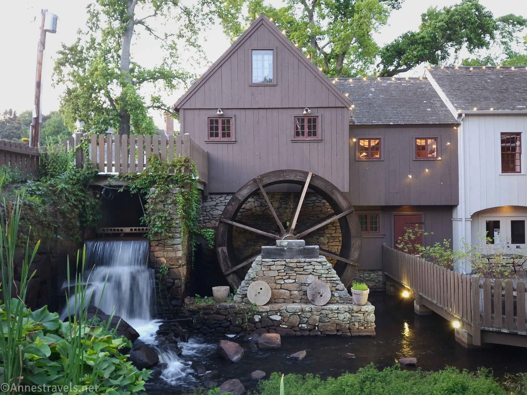 A brown grist mill with a water wheel and a waterfall with night lighting 