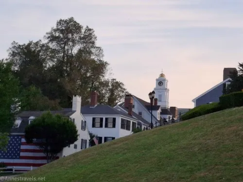An American flag on the side of a  building, white houses, trees, and a sunset