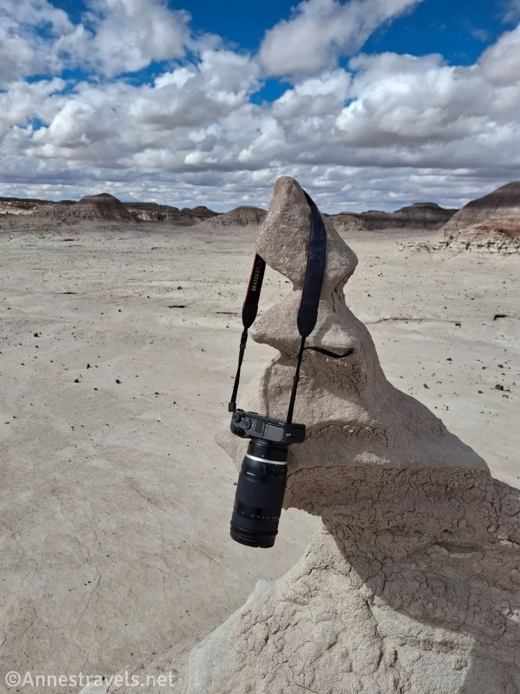 A camera hangs from a rock formation below a blue sky with puffy clouds