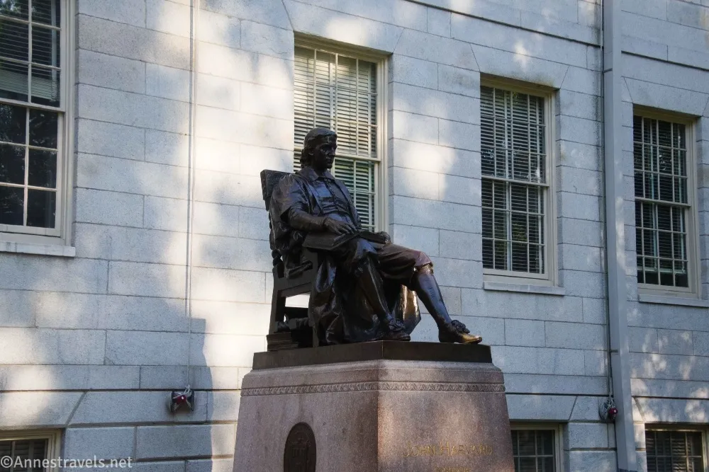 A statue of a colonial figure with a white stone building wall with windows in the background