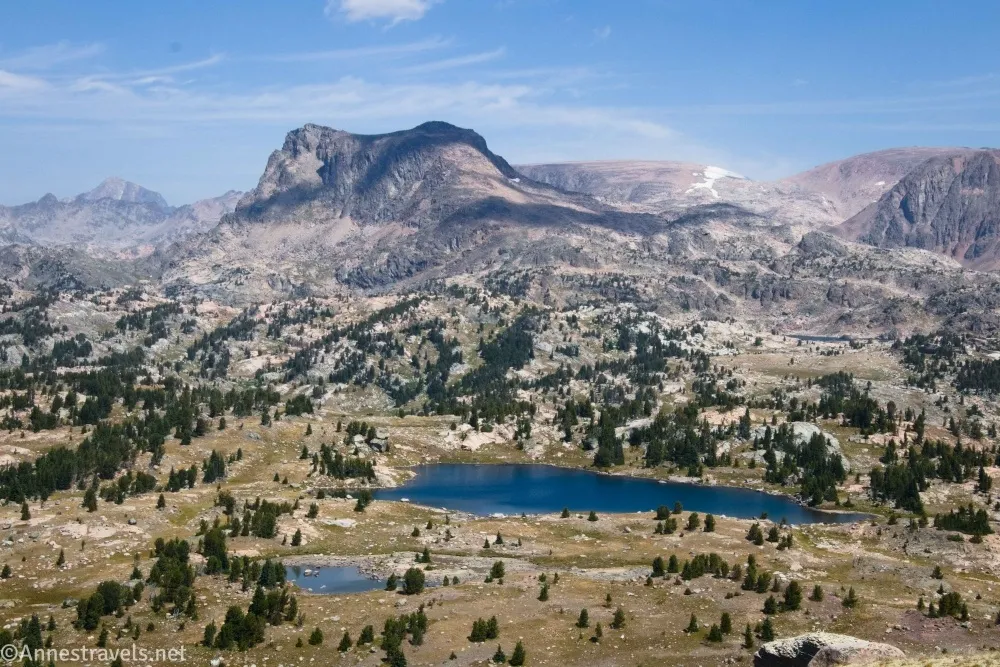Mountains rise steeply beyond meadows and two blue lakes