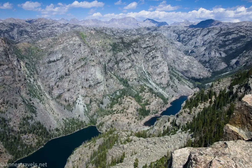 Two lakes in a valley framed by gray cliffs and distant mountains and clouds 