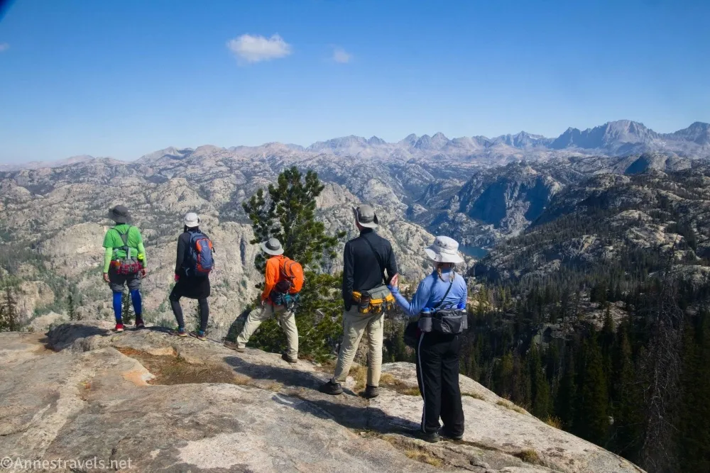 Five hikers stand on a rock looking at rocky mountains and blue skies 