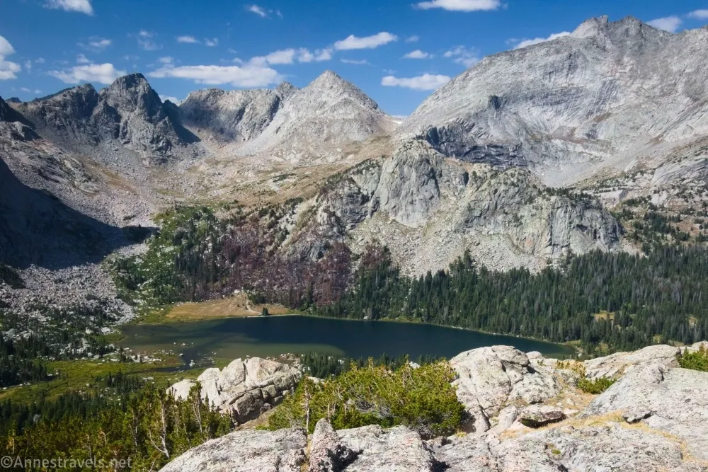 A dark blue lake is nestled below the towering cliffs of mountains 