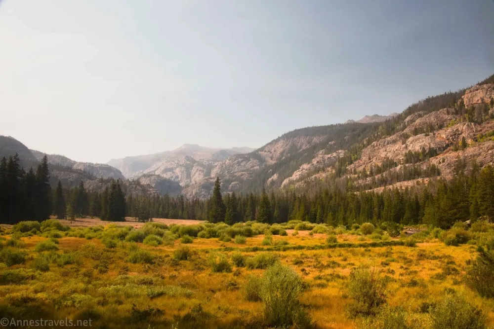A meadow with distant trees between cliffs of mountains