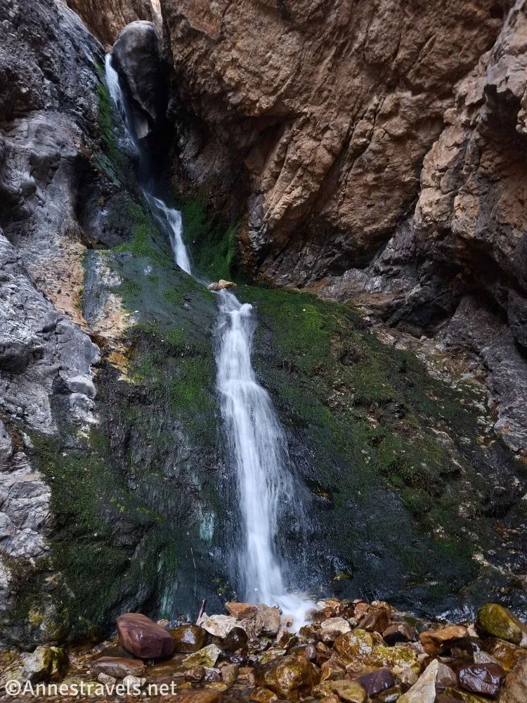 A waterfall cascades down green moss on a rocky cliff face 