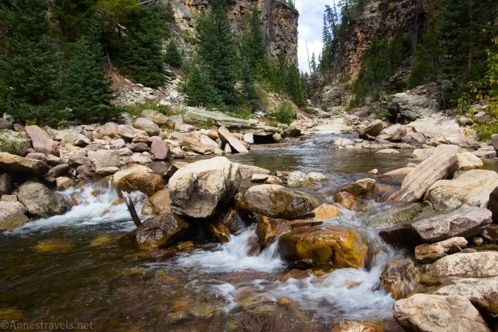 A stream tumbles over rocks in a tree-lined canyon 