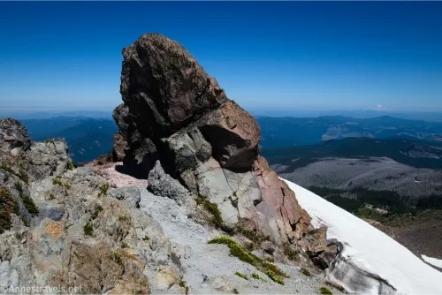 A rock pokes out of other rocks with a snowy hillside and distant mountains beyond
