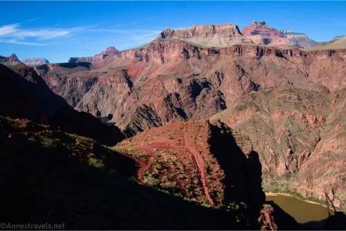 Grand Canyon cliffs rise above the Colorado River an a red trail on a hillside