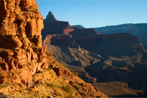 A yellow cliff illuminated in sunshine with shadowy rock formations beyond
