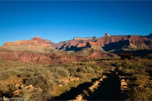 A desert plain and a shadowy trail with the cliffs of the Grand Canyon on the horizon