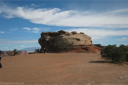 Clouds sail above a stumpy rock formation and a flat desert area