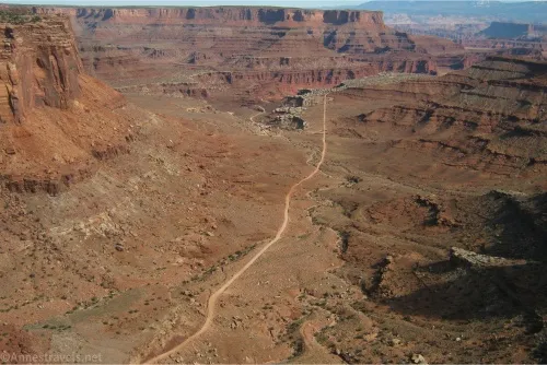 A road snakes along the bottom of a desert canyon with cliffs beyond