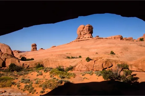 Rock formations rise out of a slickrock above sandy desert