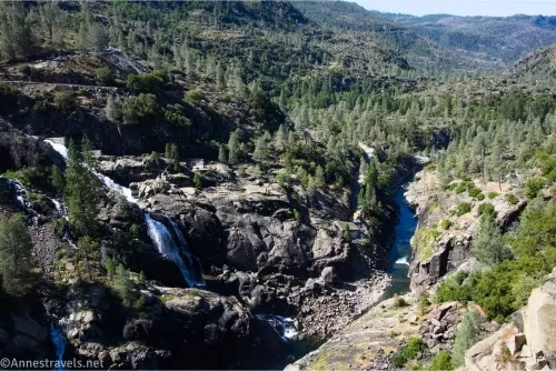 Waterfalls tumble down rocks and a blue river winds through trees