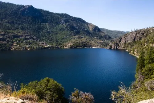 A blue lake below treed hills