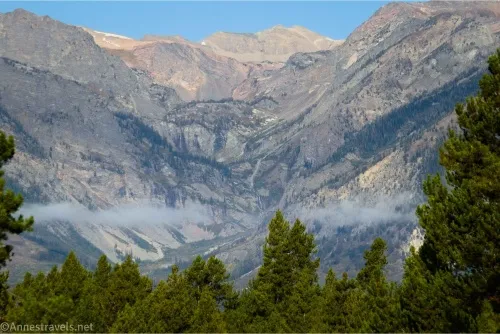Mountain cliffs rise over trees and low-hanging clouds