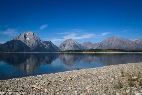 Reflections of towering peaks in a lake beyond a gravely beach