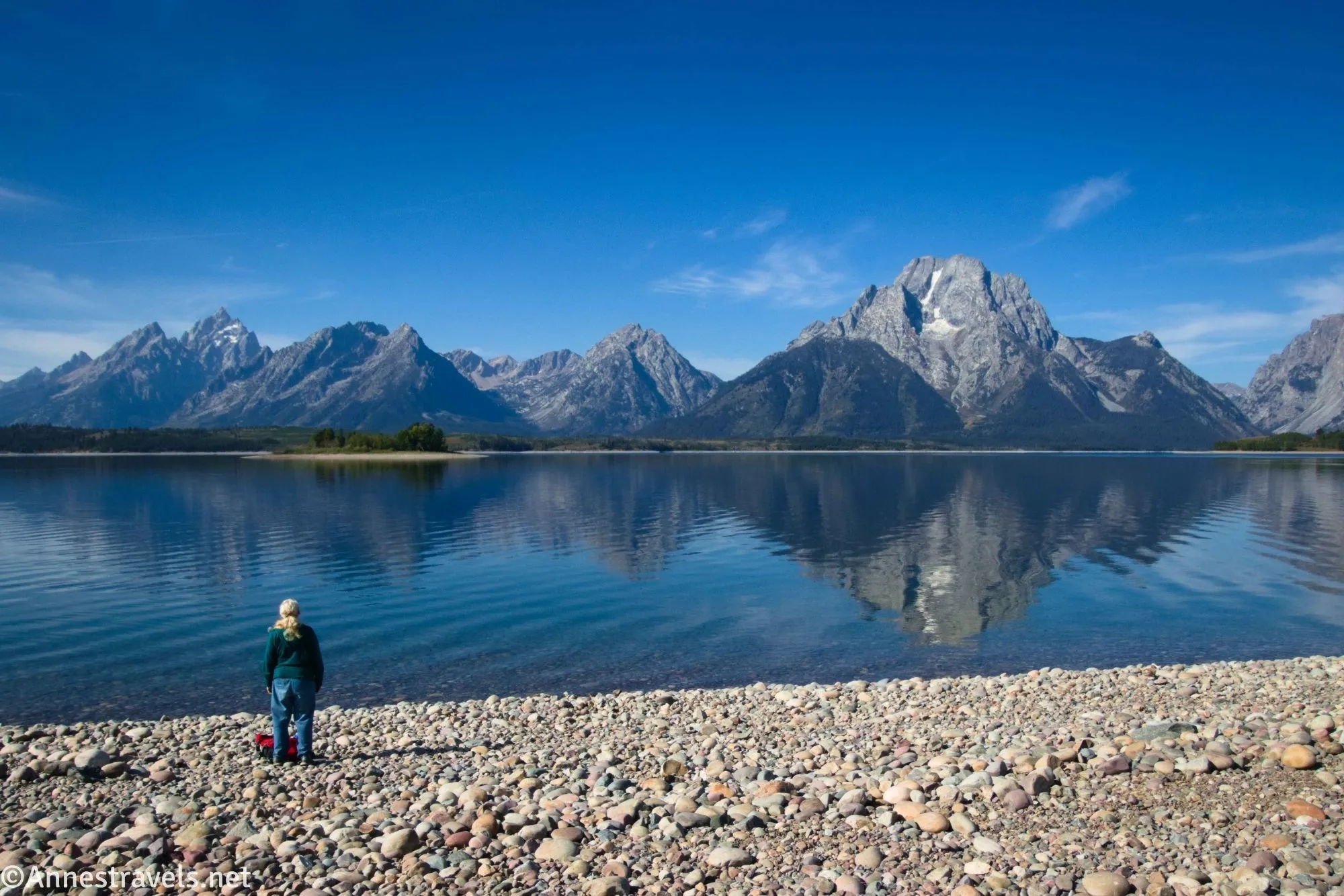 A hiker stands in awe of the reflections of the Teton Range in Jackson Lake at Hermitage Point 