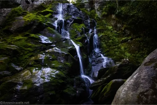 A waterfall cascades down a mossy rock face