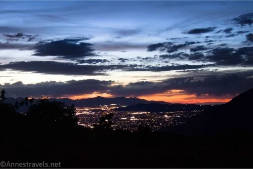 Sunset and clouds over a city with lights and a dark foreground
