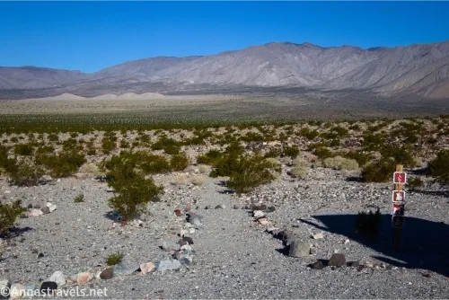 A sign and a line of rocks forms a trail into the desert that ends at mountains 