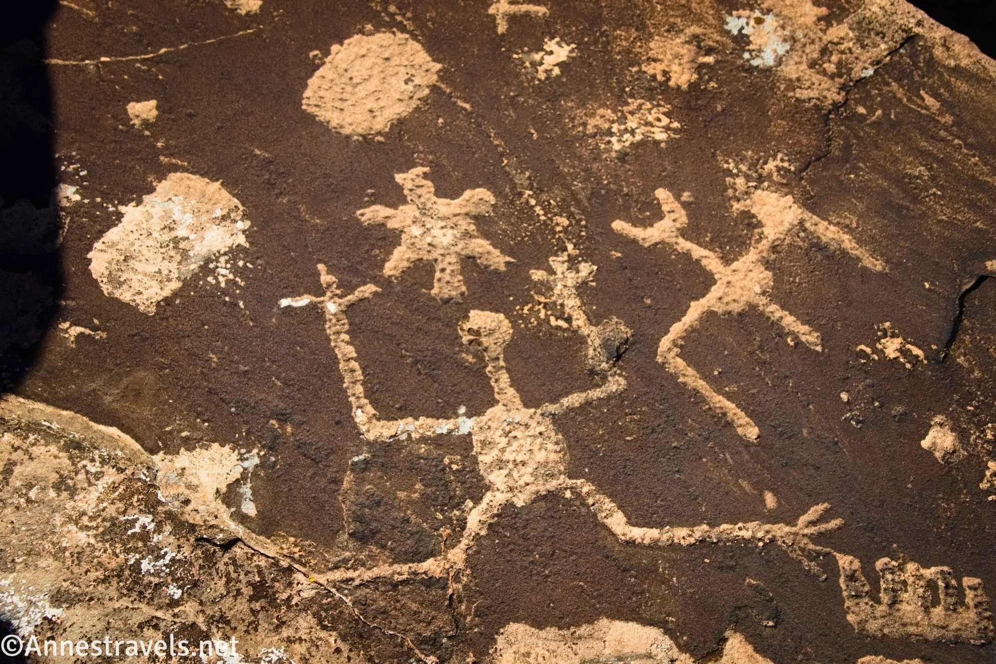 Wild figures, a sun, and more rock art on a brown boulder 